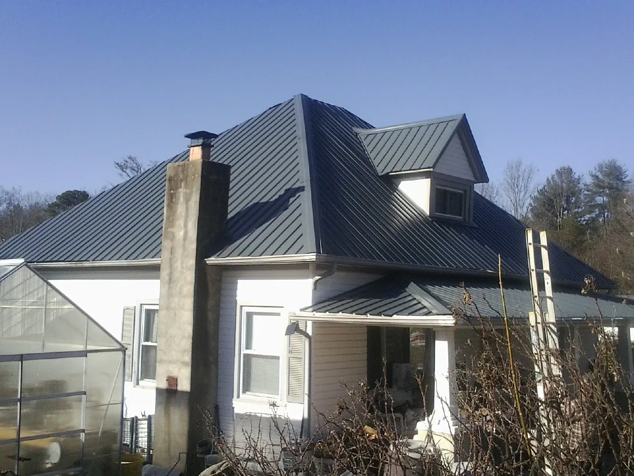 Dark blue standing seam metal roof on a white farmhouse with dormer — Slate & Tile Roof Repair by Roofing Brothers in Clifton Springs