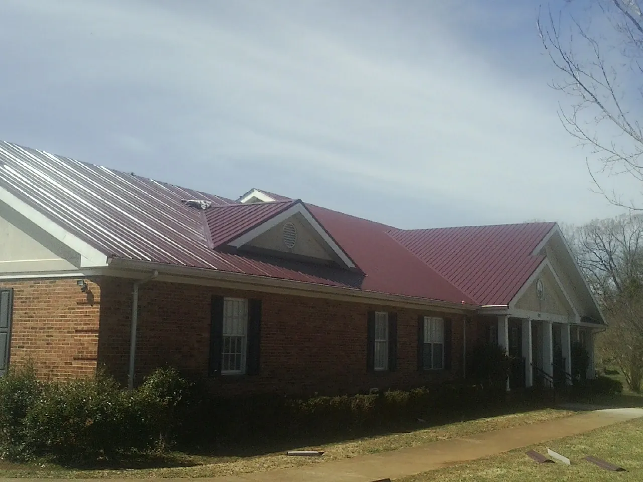 Red metal roof with gabled entries on a long brick building, from a Hail Damage Roof Repair job in Clifton Springs