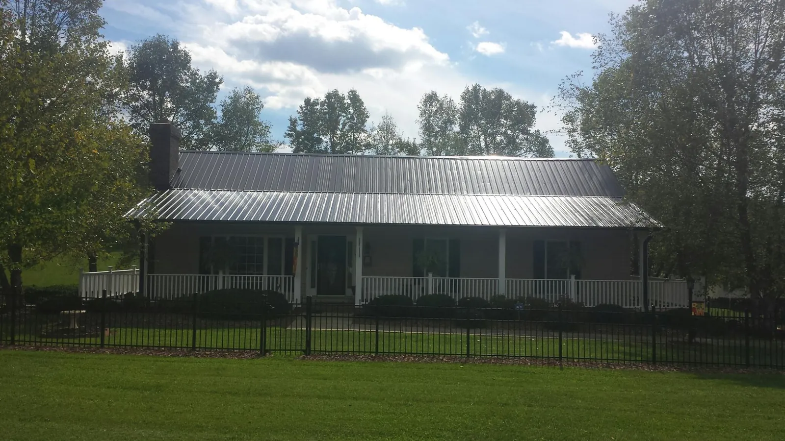 Gray metal roof on a brick ranch with a full width front porch — Gutter Guard Installation work by our crew in Clifton Springs
