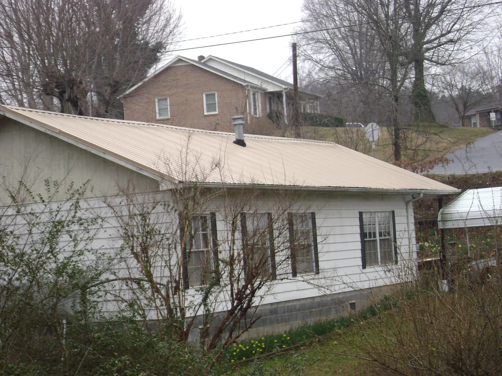 Tan metal roof on a white sided house set into a hillside — Commercial Roofing by Roofing Brothers in Clifton Springs