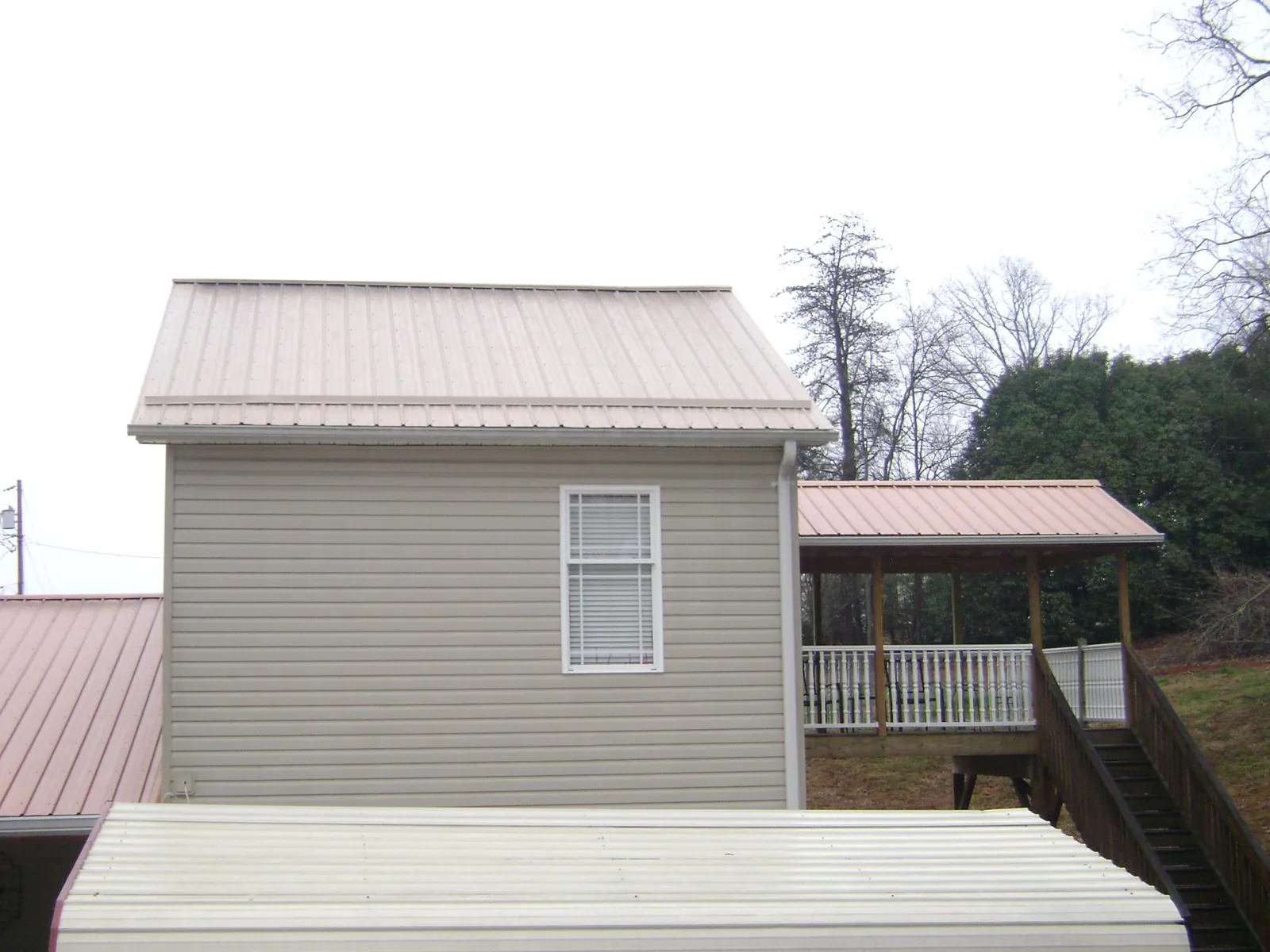 Tan metal roofs on a two story addition and attached porch, from a Roof Replacement job in Clifton Springs